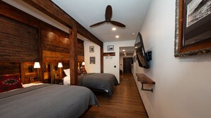 Ein Schlafzimmer mit zwei Betten, Holzböden, einem Deckenventilator und einem an der Wand montierten Fernseher.