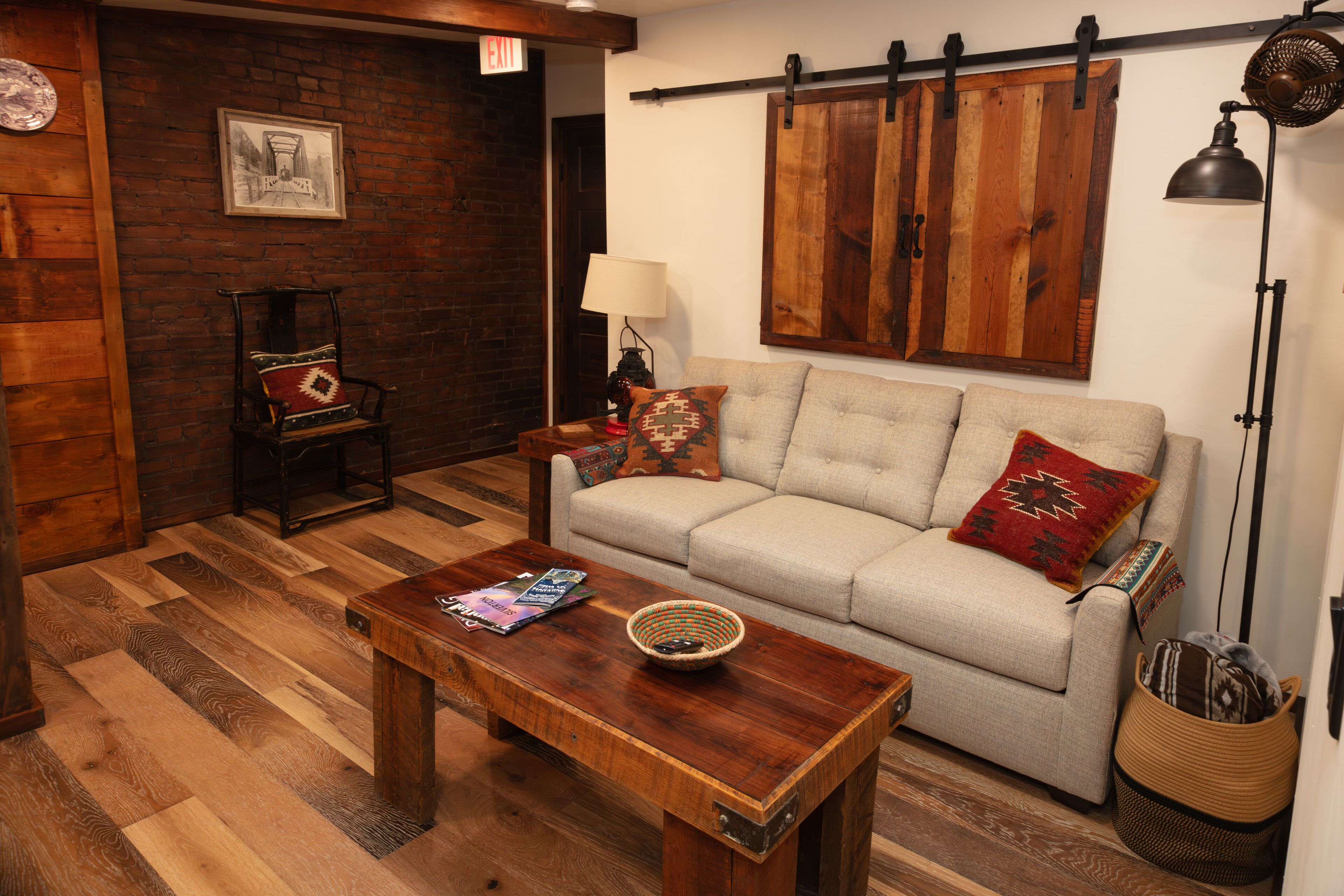 Un salón acogedor con una mesa de centro de madera, un sofá color crema con cojines estampados, una cesta de mimbre y un revestimiento de madera rústica.