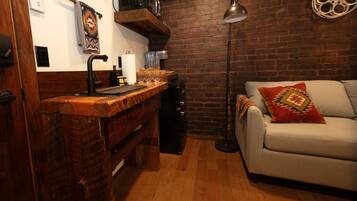 Une cuisine avec un plan de travail en bois, un évier et une machine à café. On y trouve un mur en briques et un canapé agrémenté d’un coussin décoratif.