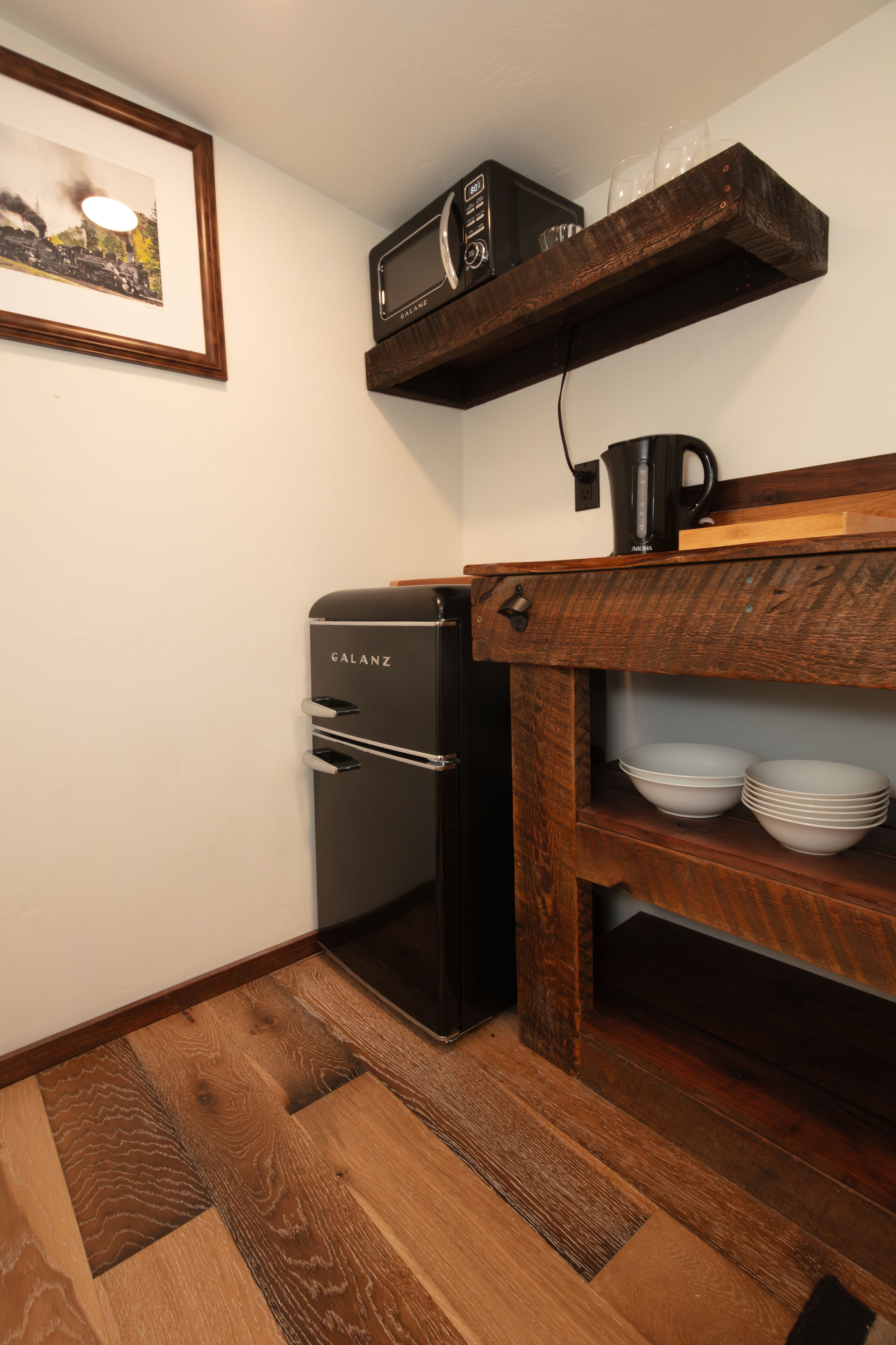 A compact kitchen with a refrigerator, a microwave, and a coffee maker on a wooden shelf.