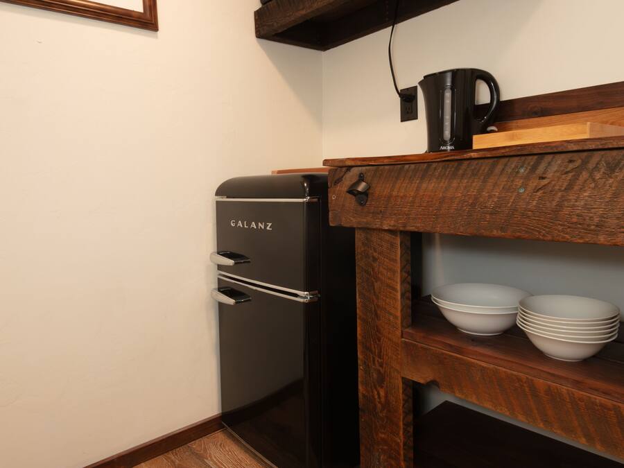 A compact kitchen with a refrigerator, a microwave, and a coffee maker on a wooden shelf.