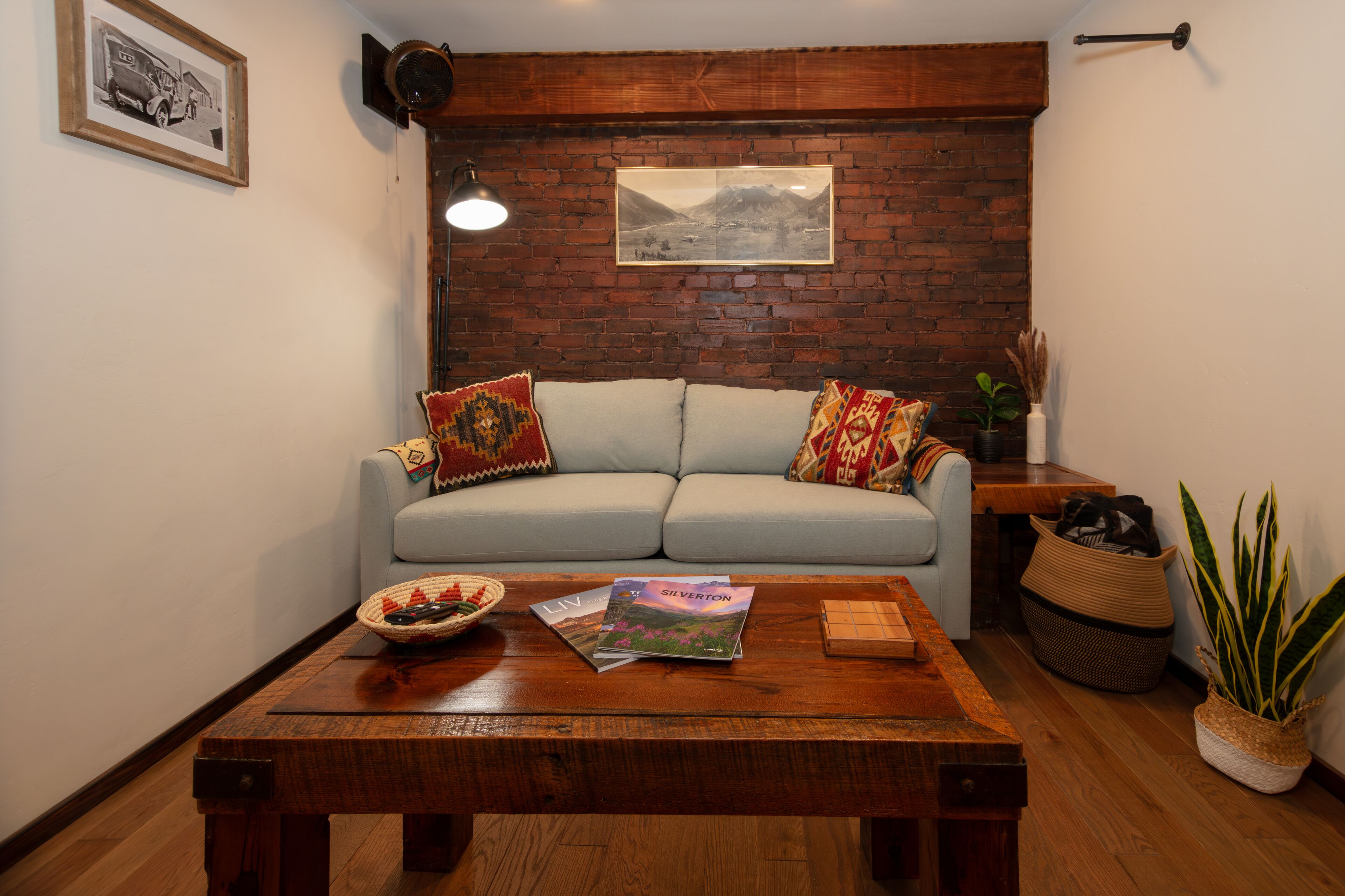 A living room with a light blue sofa, a wooden coffee table with magazines, a framed picture on the wall, and a potted plant.