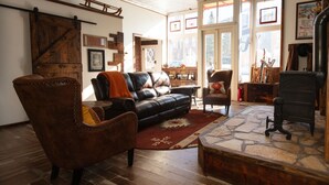 Ein gemütliches Wohnzimmer mit einer Ledersofa, einem braunen Sessel, einem Kamin aus Stein und einer rustikalen Holztür.