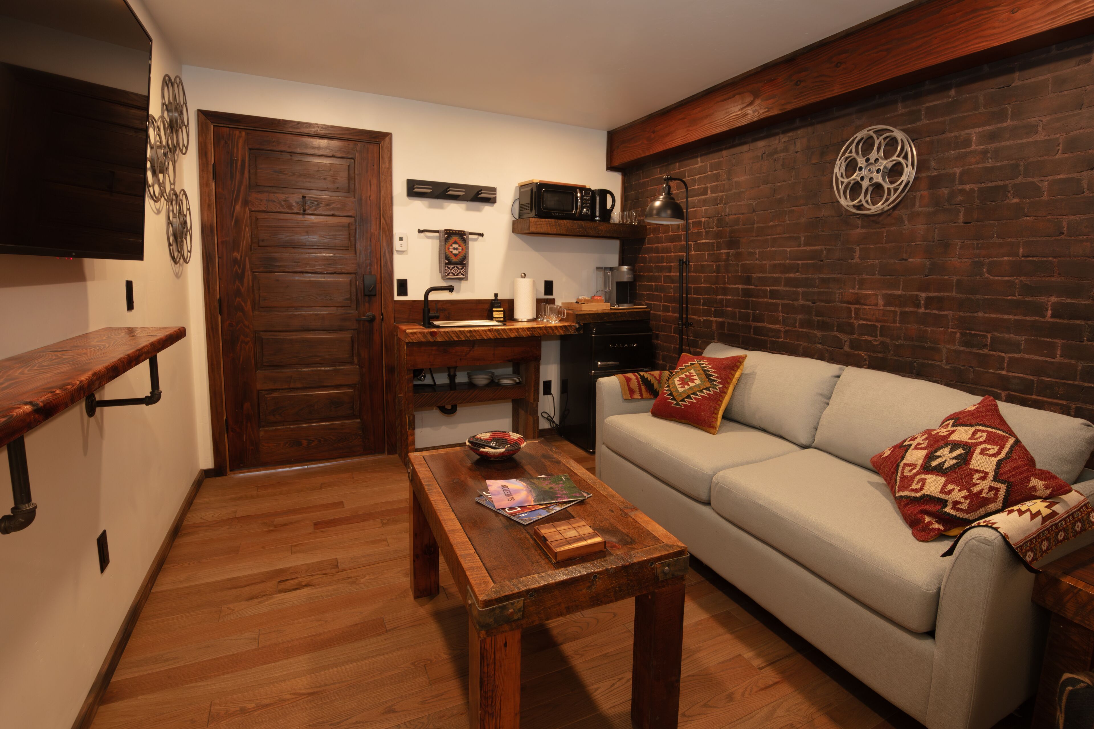 Ein gemütliches Wohnzimmer mit Couchtisch aus Holz, einer Couch mit gemusterten Kissen und einer Ziegelwand.