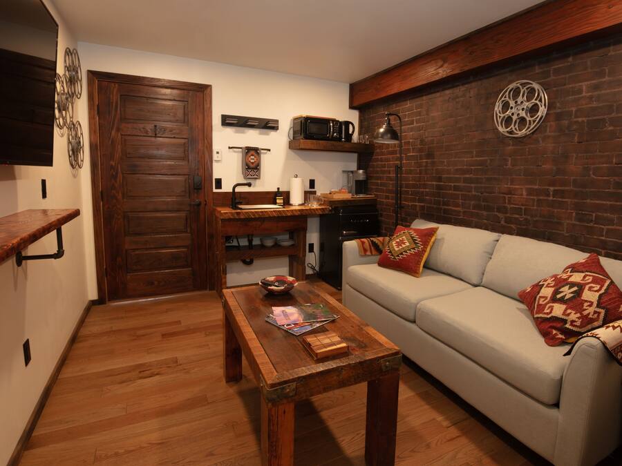 Ein gemütliches Wohnzimmer mit Couchtisch aus Holz, einer Couch mit gemusterten Kissen und einer Ziegelwand.