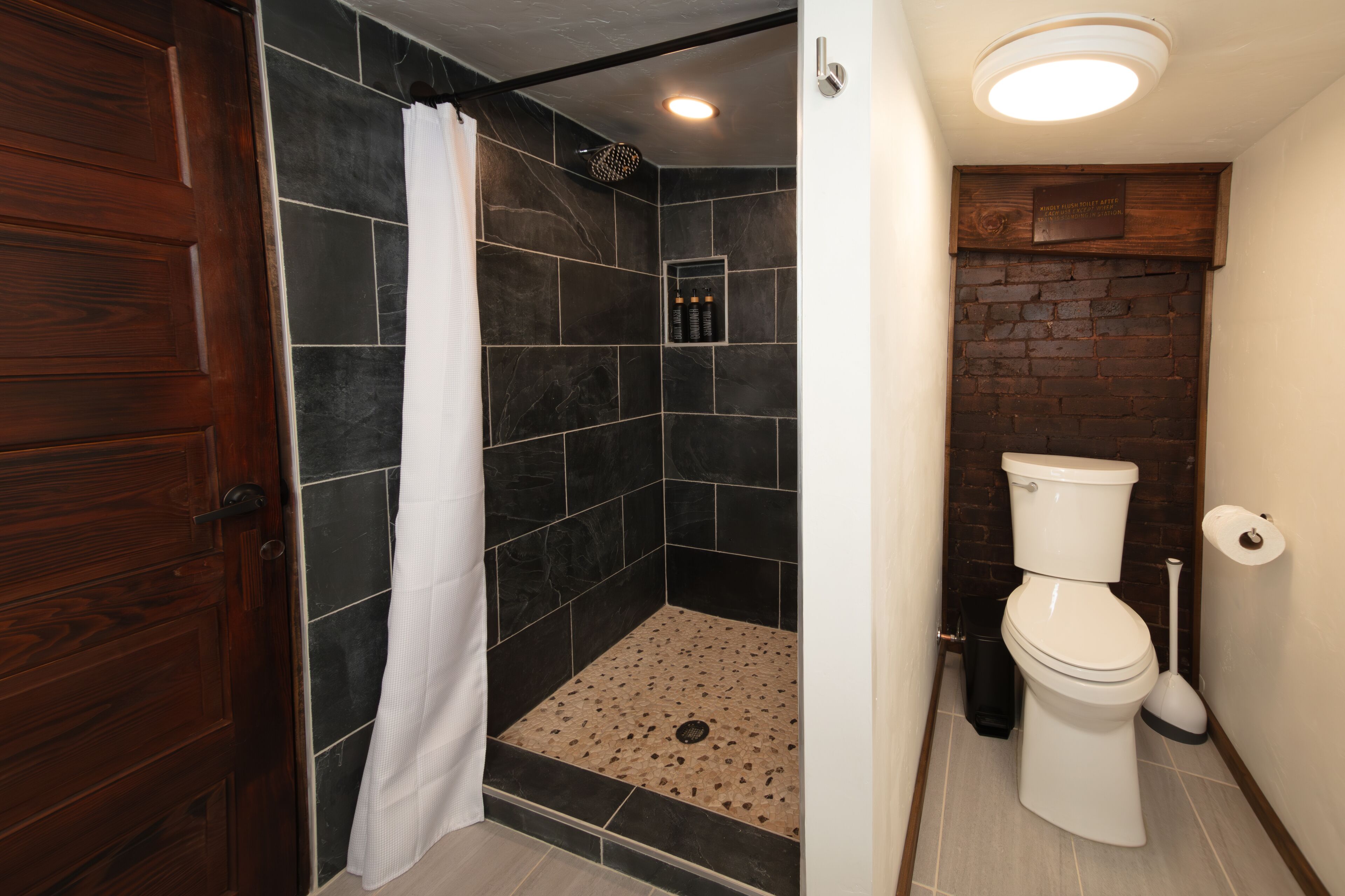 Un baño con ducha, inodoro y puerta de madera.