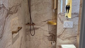 Et moderne badeværelse med marmorvægge, en bruseniche, toilet og et vaskeskab med spejl.