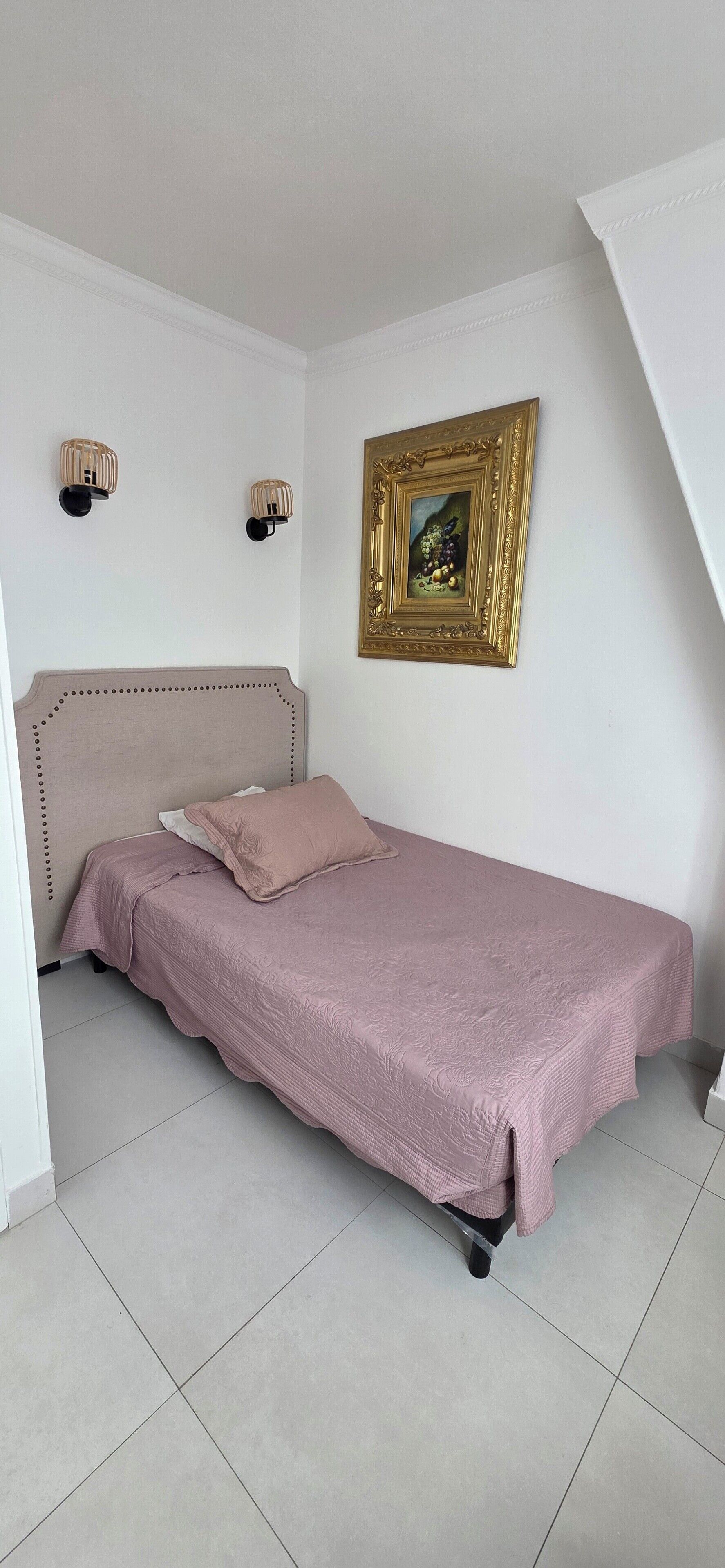 Un lit simple avec une tête de lit, un cadre photo fixé au mur et deux appliques murales.