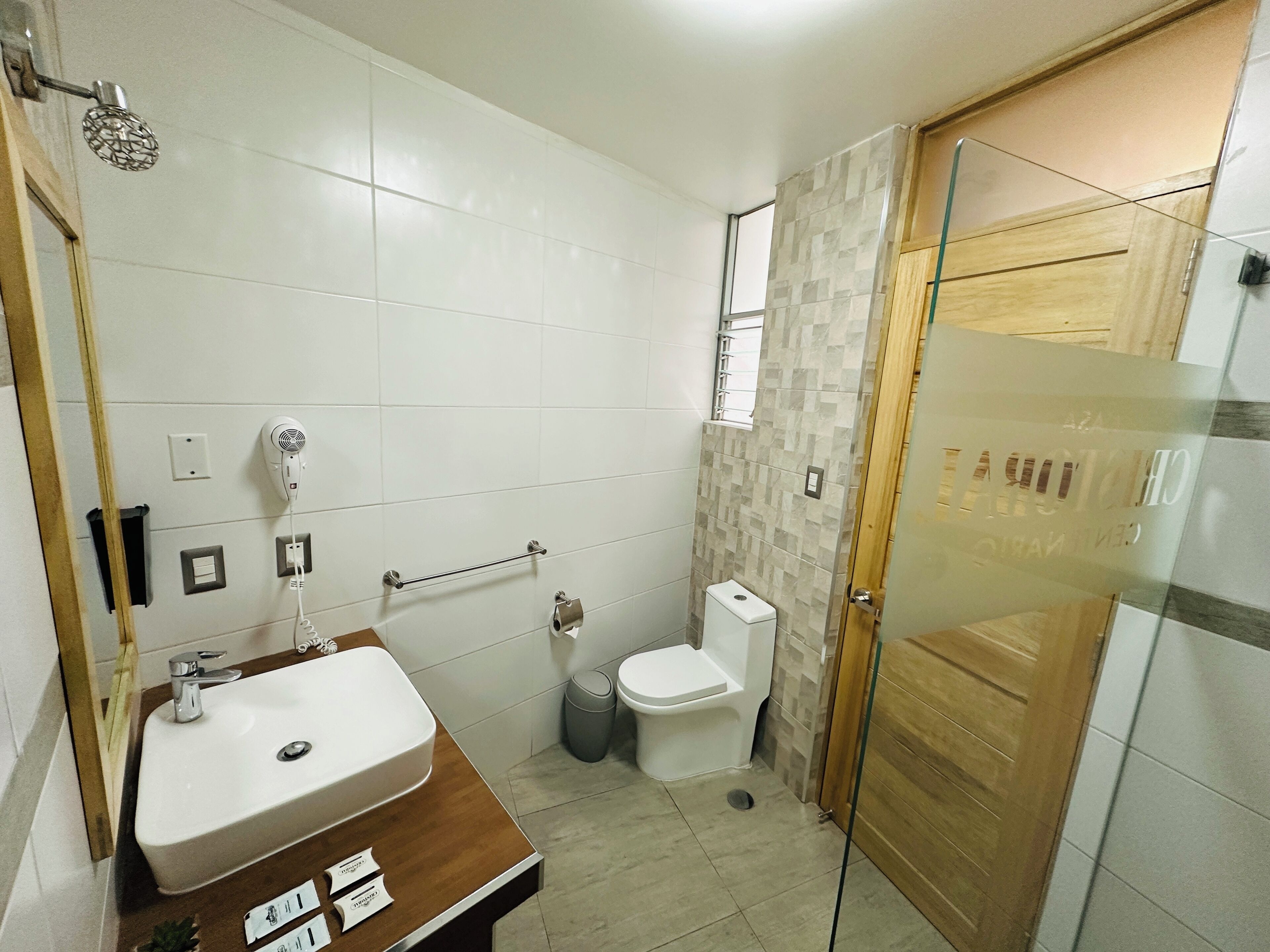 Een badkamer met een witte wastafel, een spiegel, een haardroger, een handdoekhouder, een toilet en een douche met een glazen deur.
