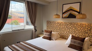 Une chambre d’hôtel avec un grand lit, une vue sur la ville par la fenêtre et une tête de lit en bois originale.