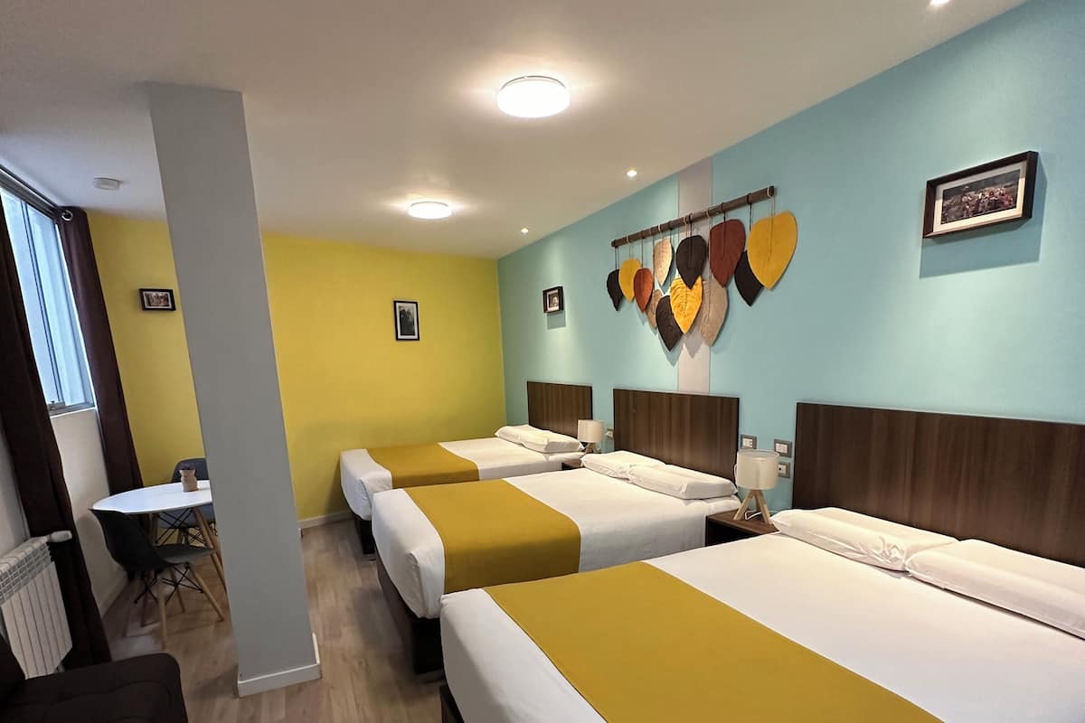 Habitación de hotel con tres camas, una zona de comedor y vistas a la ciudad.