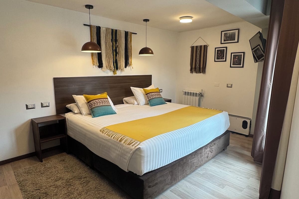 Un dormitorio moderno con una cama grande, dos mesitas de noche, una lámpara colgante y un radiador.