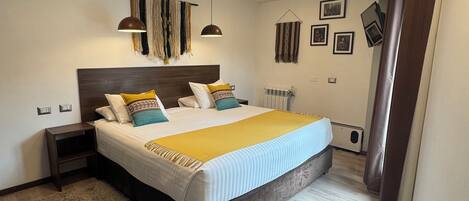 A modern bedroom with a large bed, two bedside tables, a hanging light fixture, and a radiator.