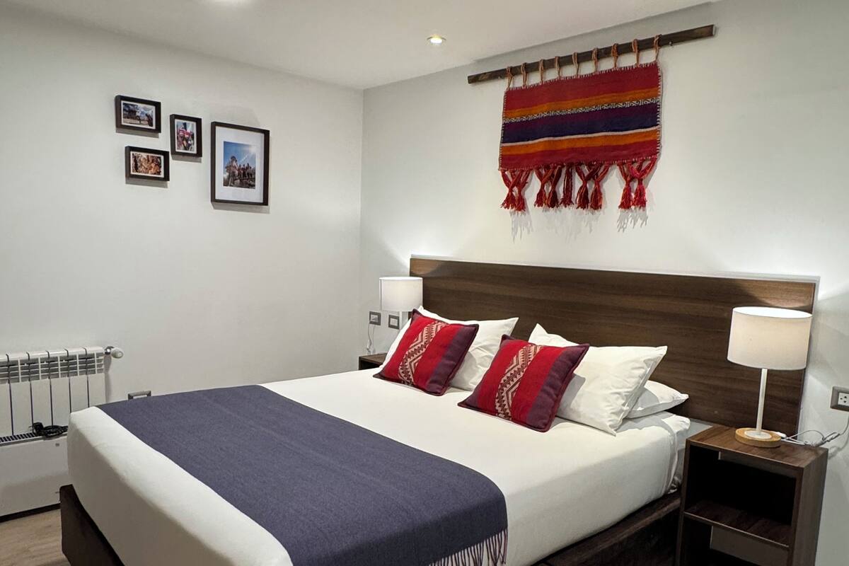 Un dormitorio moderno con una cama grande, cabecero, mesitas de noche, un tapiz colgado en la pared y fotografías enmarcadas.