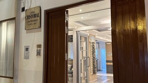 L’entrée d’un hôtel, avec une porte en bois, une enseigne indiquant « Casa Cristobal Centenario Cusco – Pérou », et un intérieur moderne doté d’un sol carrelé et d’une porte en verre donnant sur une chambre.
