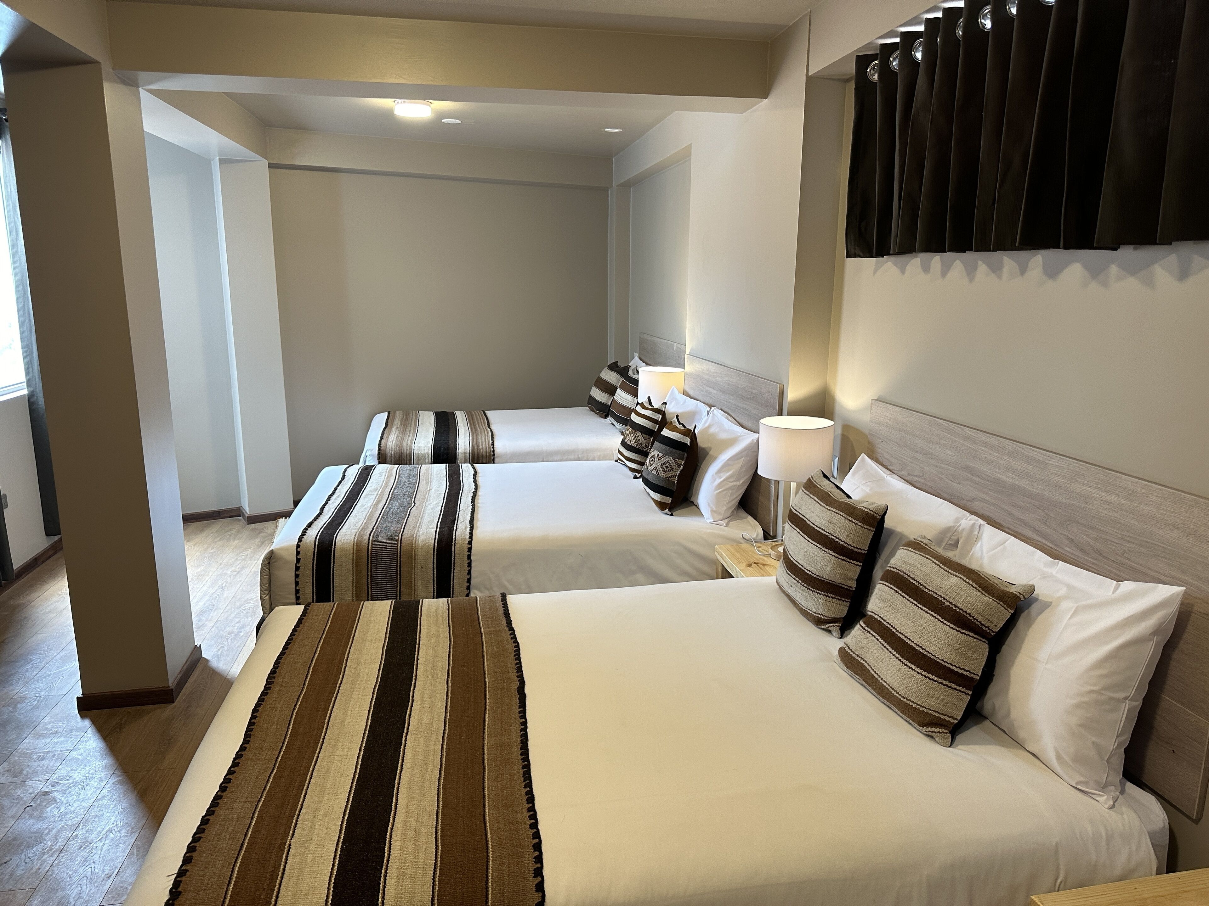 Une chambre d’hôtel avec deux lits, une tête de lit en bois, une table de chevet avec une lampe et une grande fenêtre.
