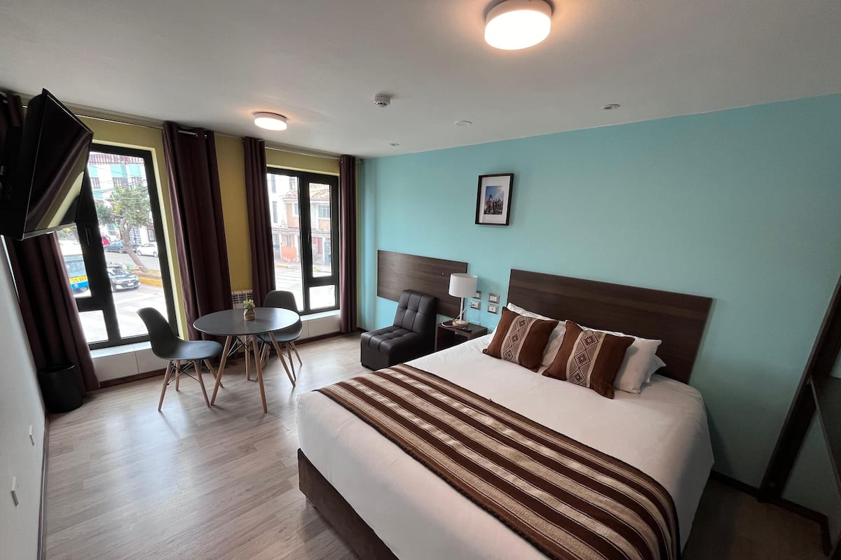 Habitación de hotel con una cama grande, un escritorio, una silla y vista a la calle por la ventana.
