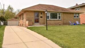 A single-story brick house with a front garage, a lawn, and two lawn chairs. - Warm spacious midsize home w/ comfort and fun (Glendale)