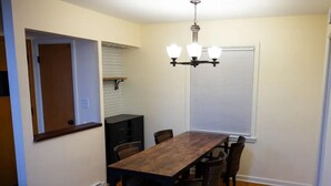 A dining area with a wooden table and chairs, a chandelier, a window with blinds, and a kitchen area in the background. - Warm spacious midsize home w/ comfort and fun (Glendale)