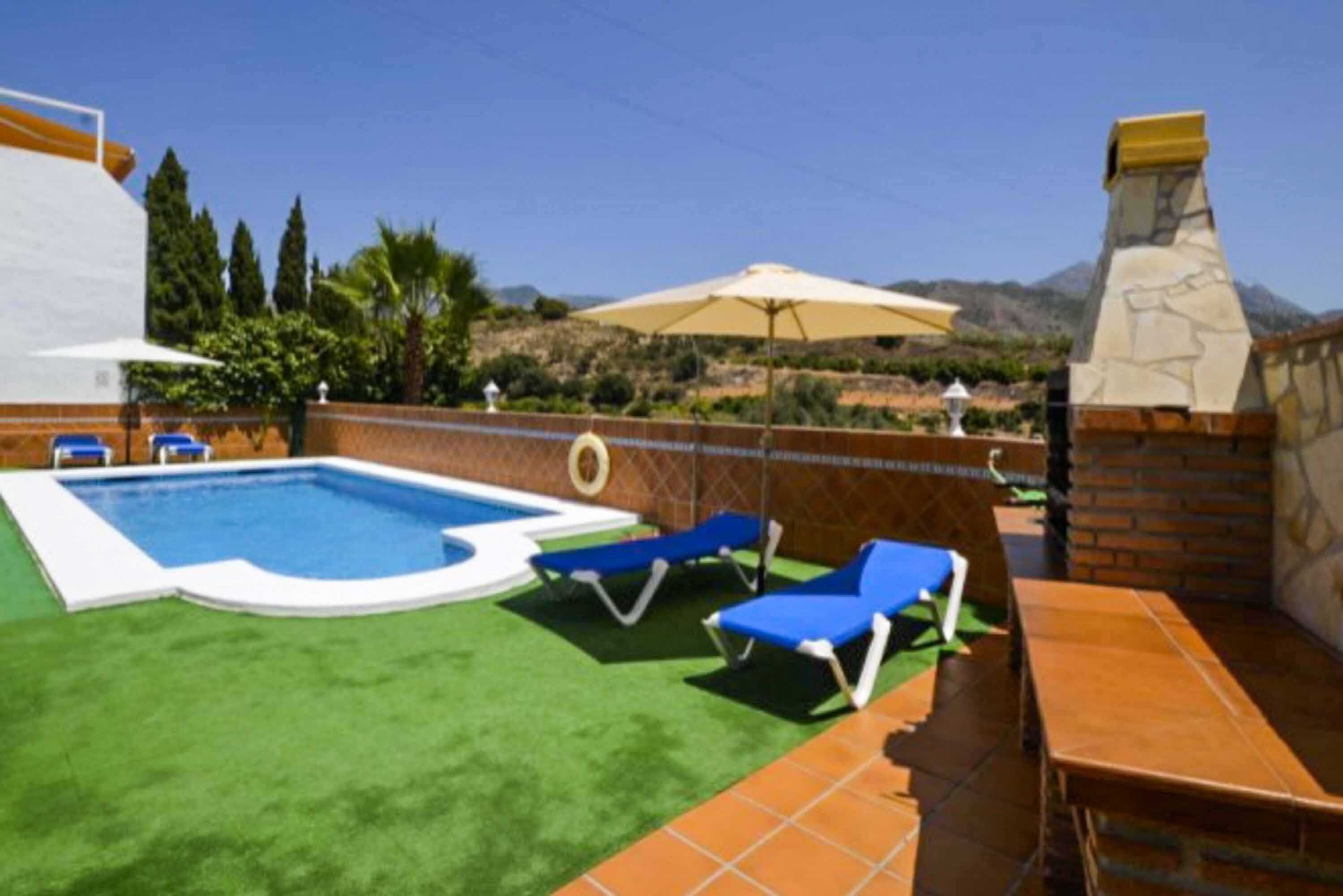 Une piscine entourée d’un mur de briques et de verdure, avec des chaises longues bleues et une table à proximité.