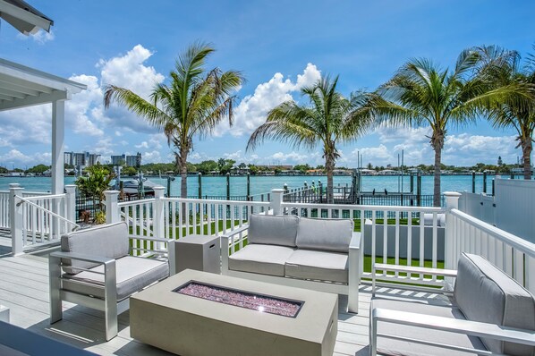 A deck with white railings, outdoor seating, and a view of the ocean.