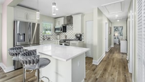A modern kitchen with stainless steel appliances, a white island, and tufted bar stools.