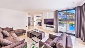 Un soggiorno moderno con un divano componibile, un tavolino e una TV a schermo piatto. Si vede una grande finestra con vista su una piscina e degli edifici.