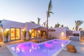 Ein moderner Poolbereich mit Liegestühlen und Sonnenschirmen, einer Steinmauer und einer gut beleuchteten Innenarchitektur.