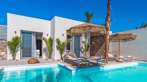 Un área de piscina moderna con piscina azul cristalina, sillas de descanso y una sombrilla de paja.