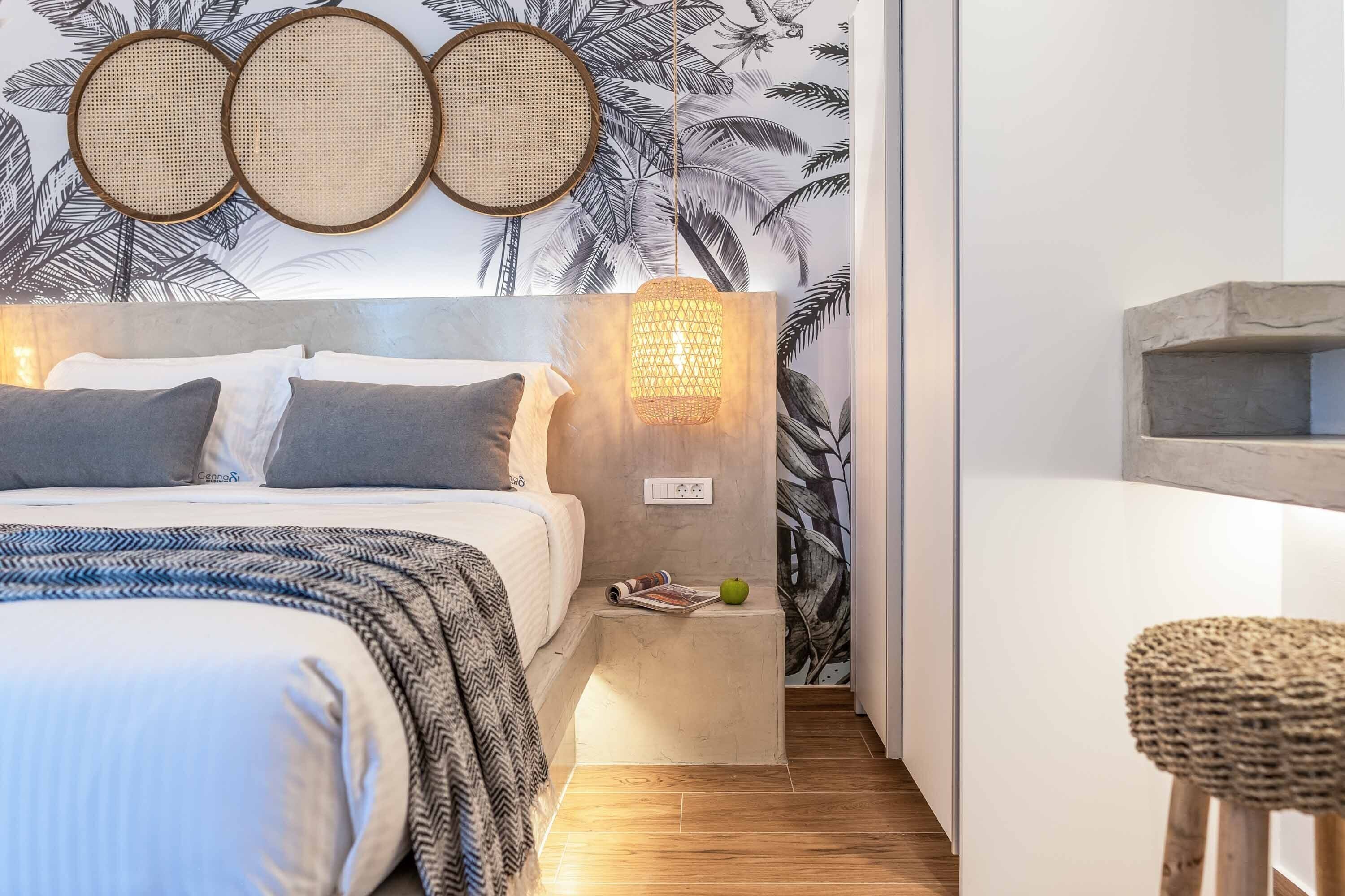 Ein Schlafzimmer mit Bett, Nachttisch, Lampe und einer Wand mit tropischem Blattmuster.