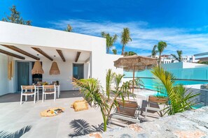 En moderne udendørs terrasse med pool, spiseplads og liggestole.