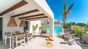 Un patio al aire libre con una mesa de comedor, sillas y una mecedora colgante. Se ve una piscina al fondo.