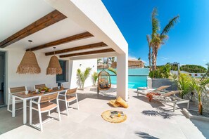 Eine Terrasse im Freien mit Esstisch, Stühlen und einer Hängematte. Im Hintergrund ist ein Pool zu sehen.