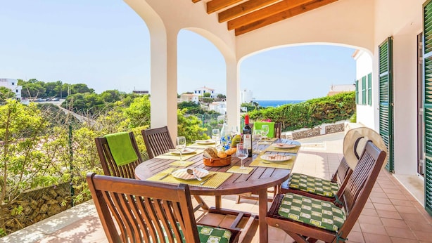 Un'area pranzo all'aperto coperta con un tavolo apparecchiato per quattro, con vista su un paesaggio suggestivo.
