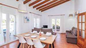 Un'ampia zona giorno con soffitto in legno, un tavolo da pranzo apparecchiato con piatti e bicchieri, un divano e un televisore.