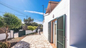 A stone-paved pathway leading to a white building with green shutters. - Villa Chiquita - Three Bedroom Villa, Sleeps 4 (Cala en Porter)