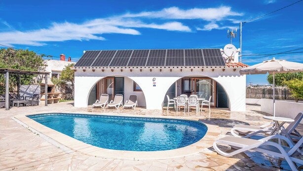 A pool area with a white building, solar panels, and lounge chairs. - Villa Chiquita - Three Bedroom Villa, Sleeps 4 (Cala en Porter)