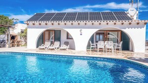 A poolside area with a white building featuring two arched doorways, each with a set of white lounge chairs. - Villa Chiquita - Three Bedroom Villa, Sleeps 4 (Cala en Porter)