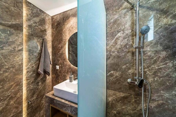 A bathroom with a marble wall, a sink, and a shower.
