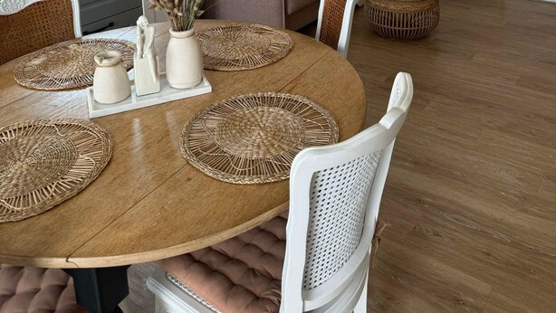 A modern kitchen with a large window, a dining area with a round table and white chairs, and a living area with a sofa and decorative wall art.