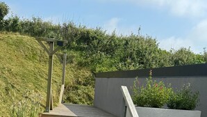 A wooden staircase leading to a deck with a view of a grassy hill.