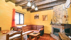 A cozy living room with a stone fireplace, wooden furniture, and a patterned sofa. - Villa Cortijo Algarrobo (Frigiliana)