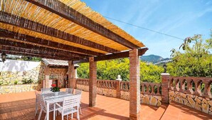 An outdoor patio with a table and chairs, a stone wall, and a view of greenery and hills. - Villa Cortijo Algarrobo (Frigiliana)