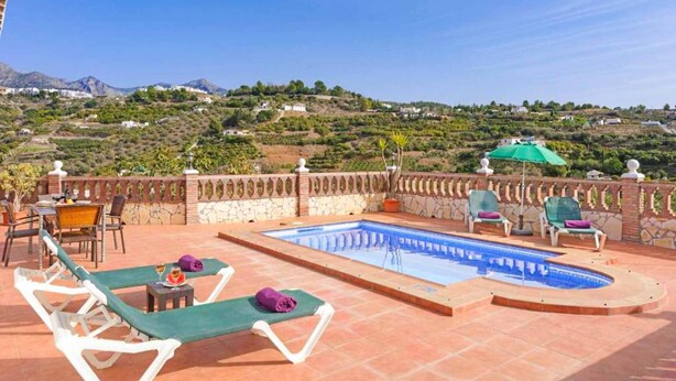 A rooftop pool area with lounge chairs, a table, and a view of a hilly landscape. - Villa Cortijo Algarrobo (Frigiliana)