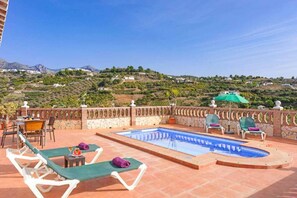 Un espace piscine aménagé sur le toit, avec des chaises longues, une table et une vue sur un paysage vallonné.