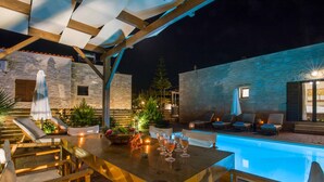 Uma área de piscina ao ar livre com espreguiçadeiras e uma mesa de jantar, cercada por paredes de pedra e plantas em vasos.
