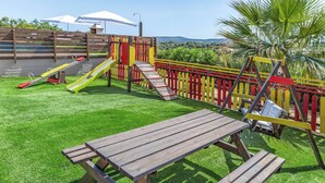 A playground with slides and swings, a picnic table, and a view of greenery and hills. - Villa Ourania Klio - Two Bedroom Villa, Sleeps 4 (Crete)