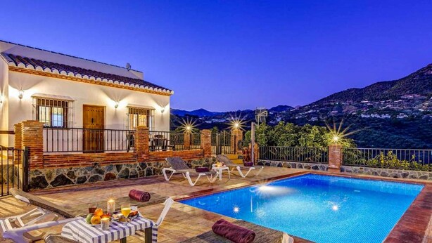 A villa with a swimming pool, outdoor seating, and a mountain backdrop.