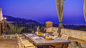 An outdoor dining area with a table set for two, overlooking a mountainous landscape at dusk.