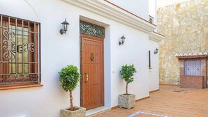 Un edificio con una puerta de madera, dos plantas en macetas y un muro de piedra.